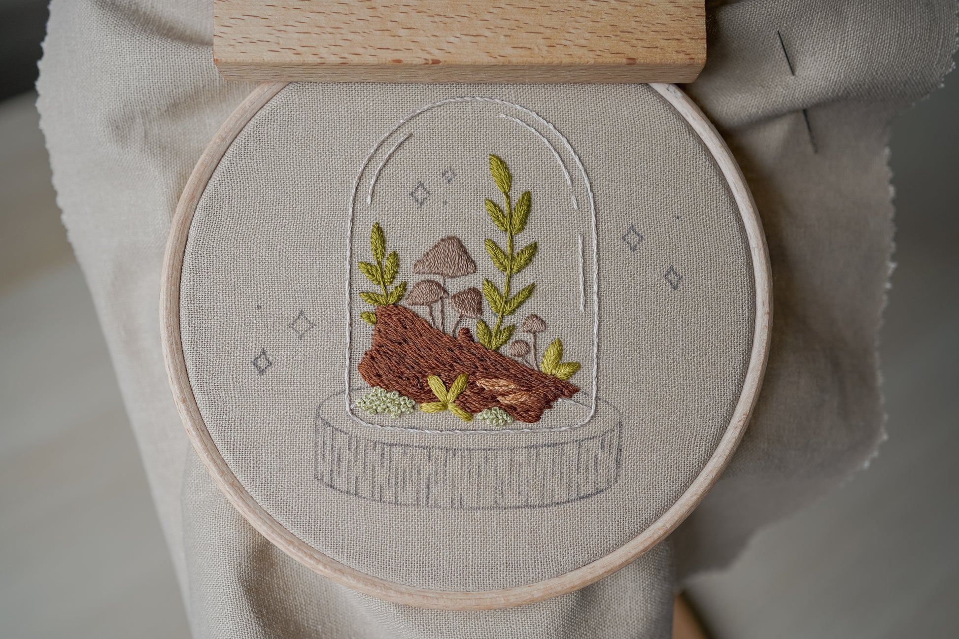 Embroidery hoop with a nature-themed embroidery design featuring mushrooms and plants on a neutral background