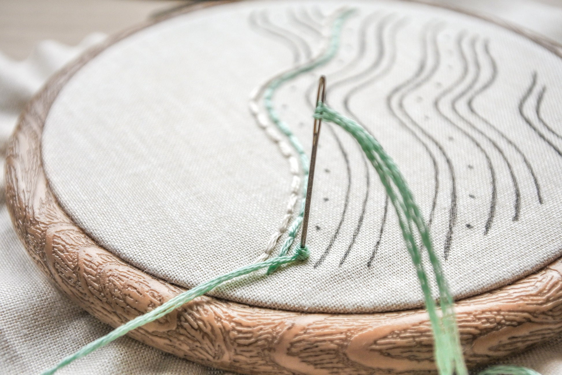 Closeup of a needle stitching a turquoise French knot on the beach wave embroidery pattern