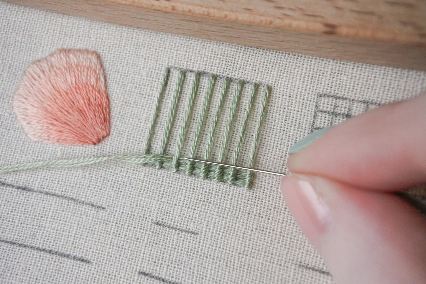 Close-up of web stitch in progress, showing the intricate woven pattern being created with pale green thread on light neutral fabric