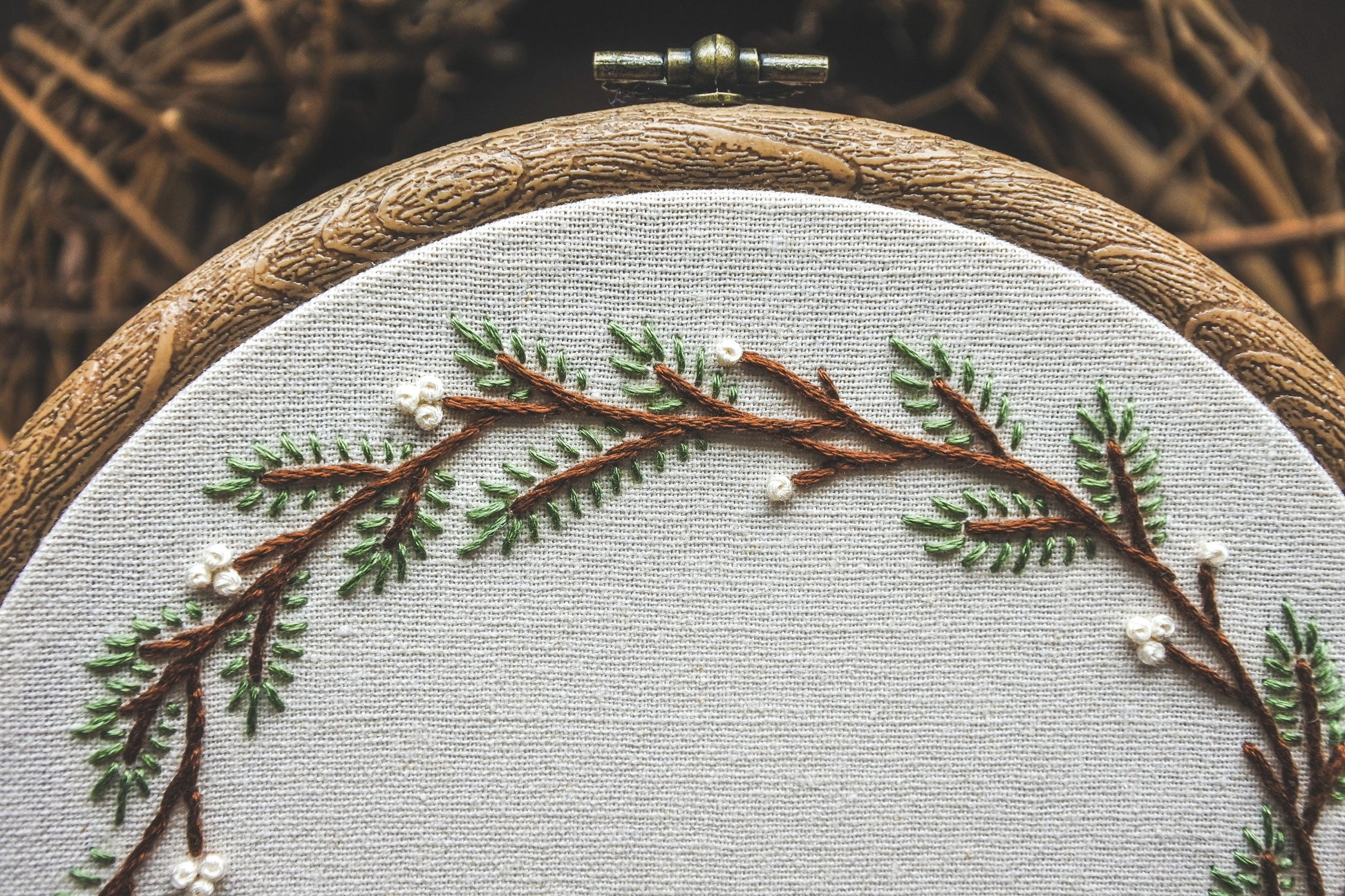 Detail of embroidered pine branches and white berries in a winter-themed hoop
