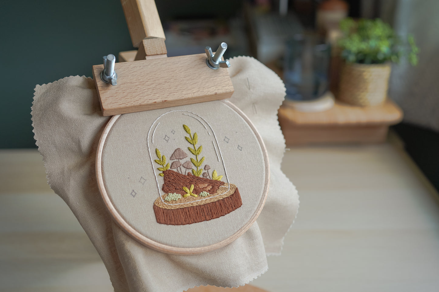 Embroidery hoop with a woodland terrarium design in a wooden hoop stand.